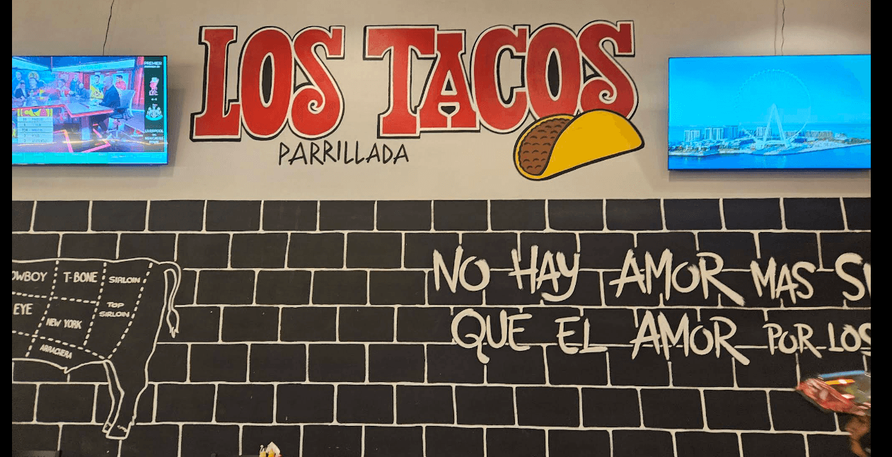 Interior de Los Tacos Parrillada con pantallas transmitiendo partidos junto al mural de la marca