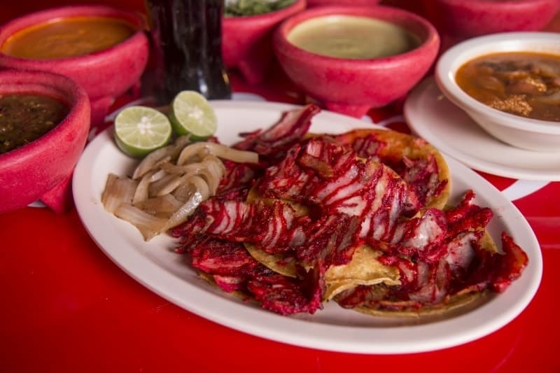 Orden de tacos de trompo con cebolla asada, limones y salsas
